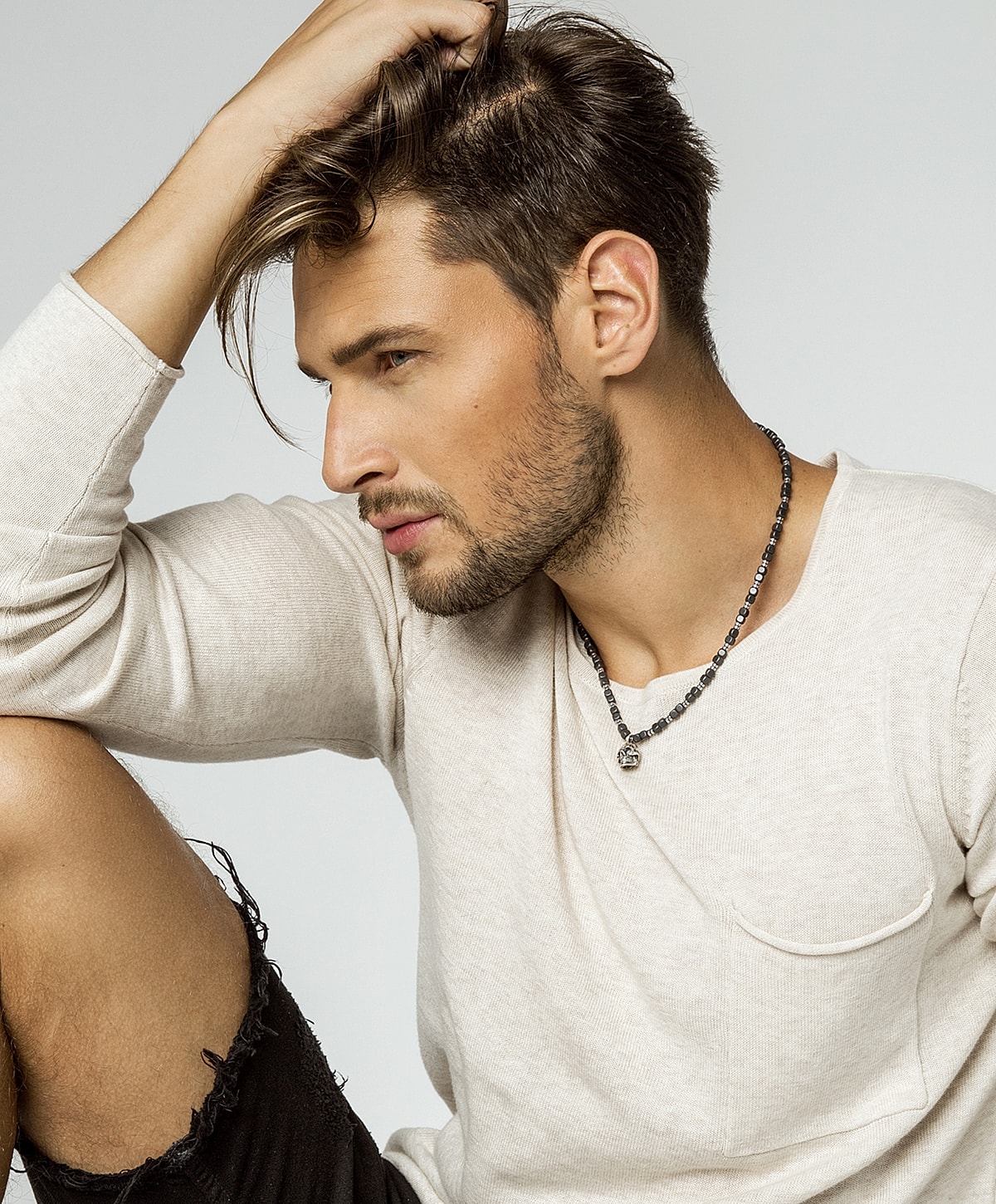 Man in casual attire, stylish necklace, thoughtful pose.