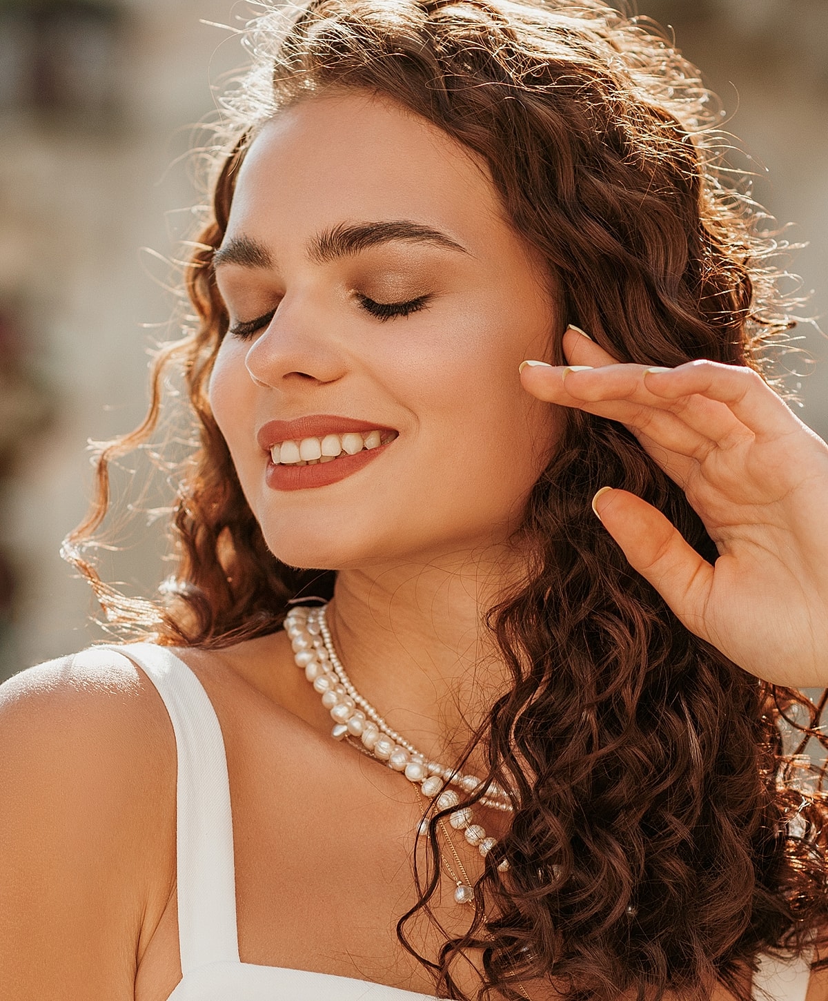 Smiling woman with curly hair and pearls.