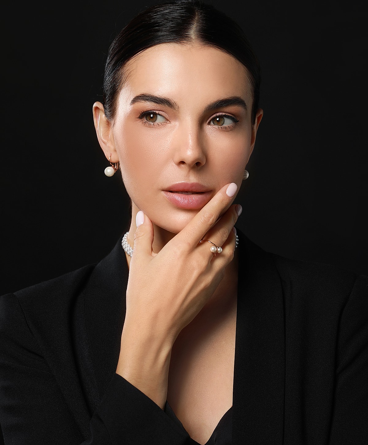 Elegant woman with pearl accessories on black background.